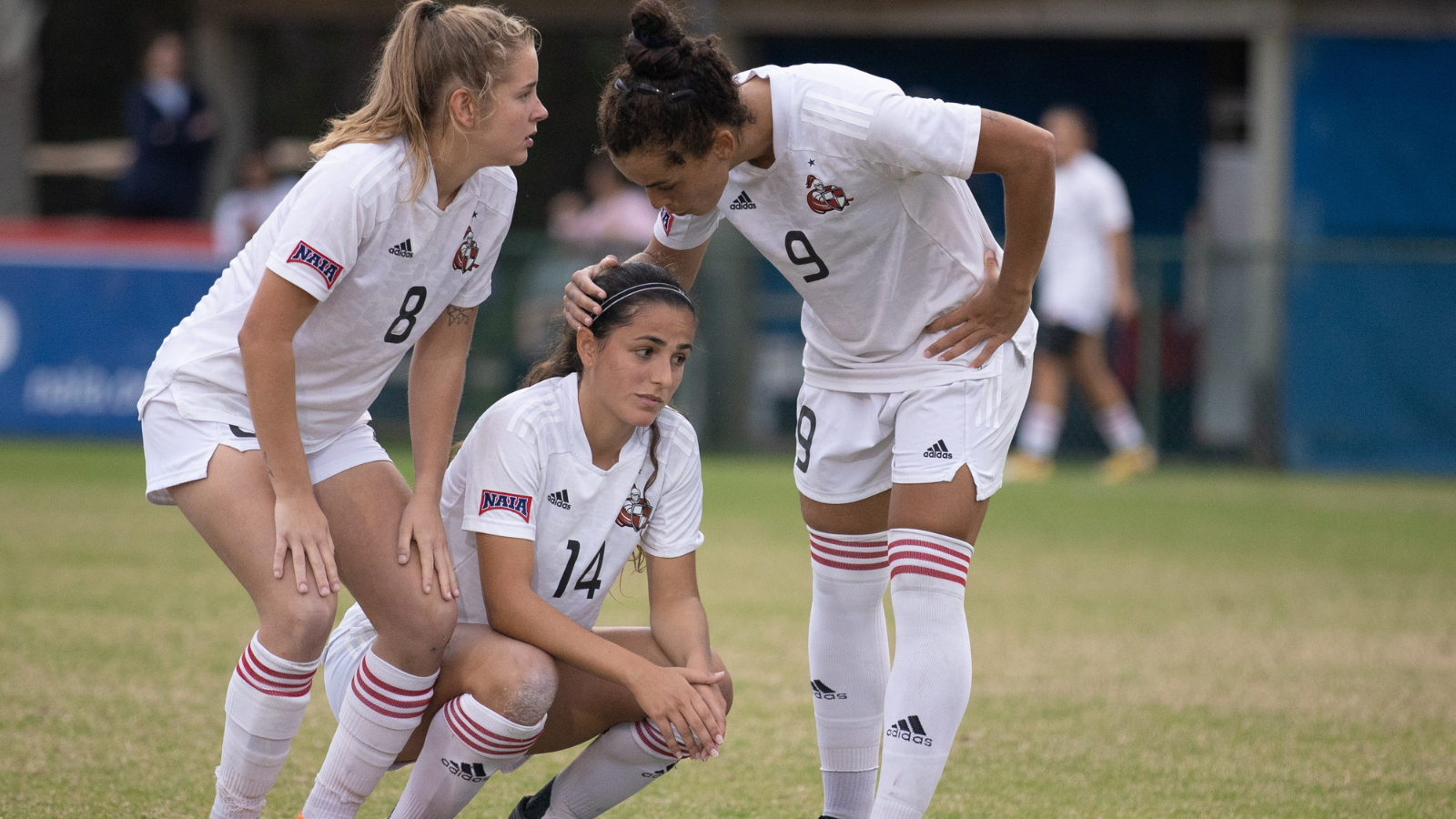 Two soccer players consulting their teammate in distress