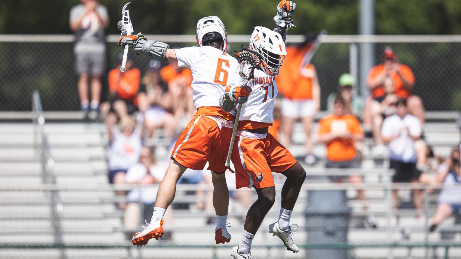 Two men’s lacrosse players jumping in celebration, wearing orange uniforms.