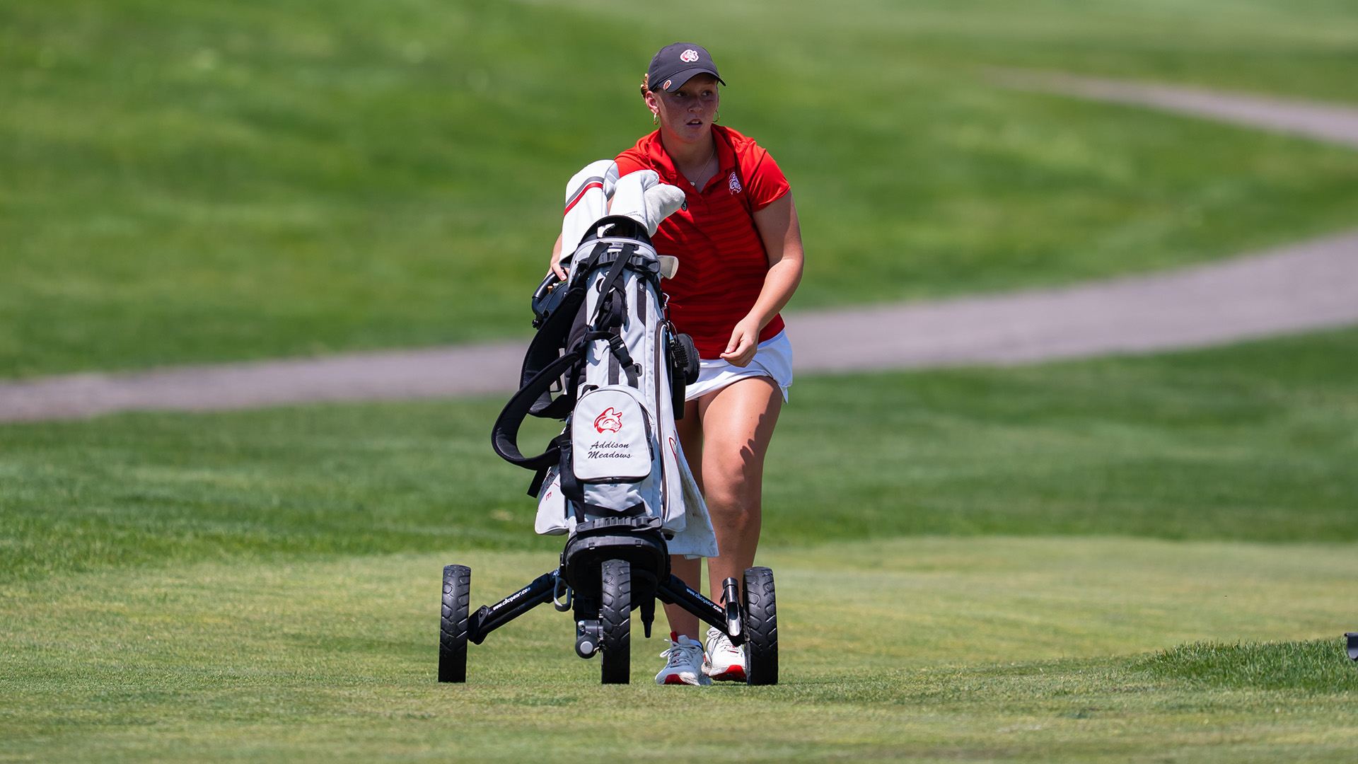 A golfer walking up the fairway pushing her golf bag.
