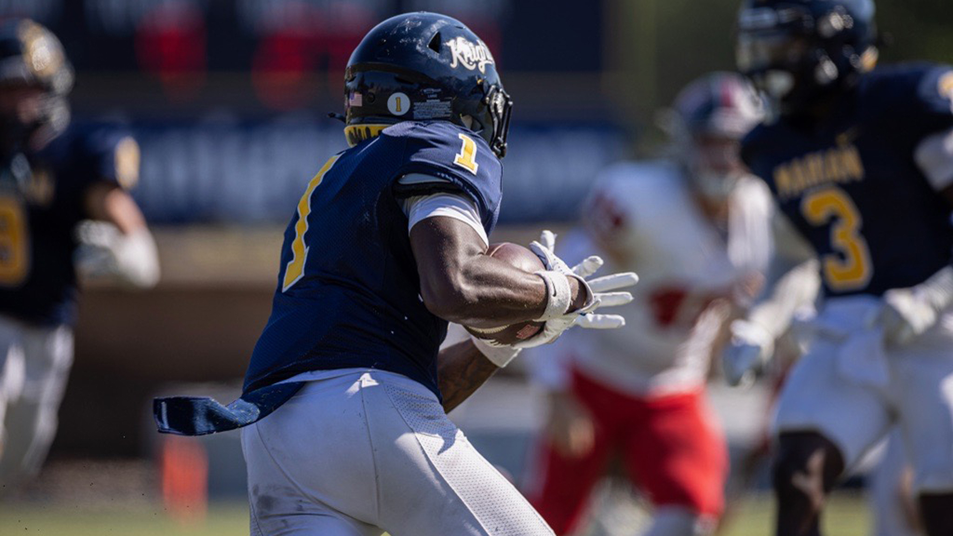 A player with his back turned running the ball in football.