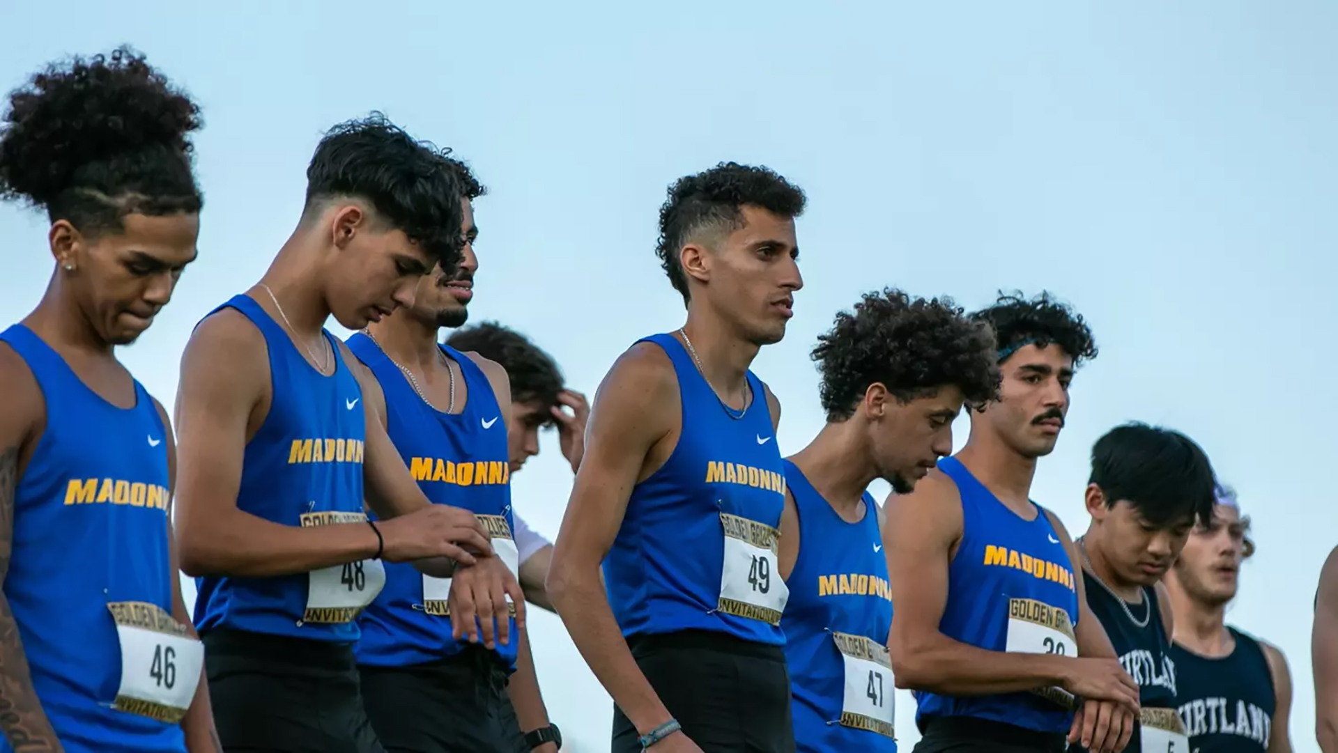 Runners line up at the start line for a collegiate cross country race.